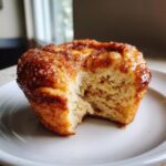 A close-up of a cinnamon sugar french toast muffins with a bite taken out, showing the soft interior.