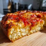 Close-up of a thick slice of baked cottage cheese pizza crust topped with bright red sauce and herbs.