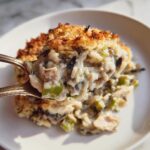 A spoonful of creamy chicken wild rice casserole with a crispy topping being lifted from the dish.