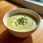 A close-up of a creamy bowl of potato leek soup, garnished with fresh chopped chives.