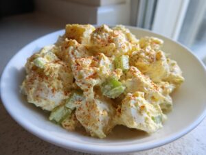 A close-up of creamy potato salad mixed with celery and topped with a dusting of paprika.