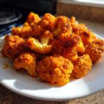 Close-up of several crispy, bright orange buffalo cauliflower florets piled high on a white plate.