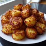 A mound of perfectly golden brown, crispy roasted potatoes with shredded edges piled on a white plate.