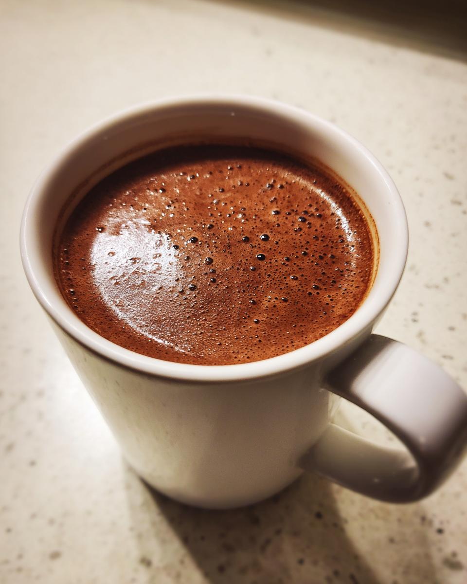 Close-up of a white mug filled with rich, frothy crockpot hot chocolate.