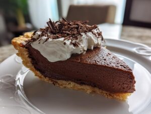 A close-up of a slice of rich french silk pie with a thick chocolate filling, topped with whipped cream and chocolate shavings.