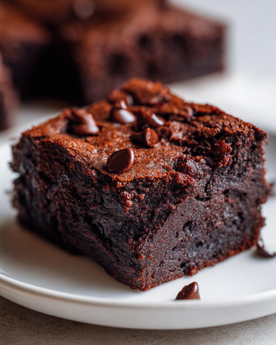 A close-up, decadent square of fudgy zucchini brownies topped with melted chocolate chips on a white plate.