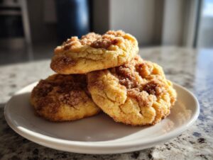 Three soft, golden Gilmore Girls coffee cake cookies stacked on a white plate, topped with cinnamon sugar.