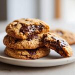 Stack of gooey peanut butter chocolate chip cookies with melted chocolate oozing out, one cookie is broken open.
