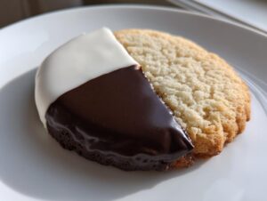 A single, perfectly iced black and white cookie, half covered in white fondant and half in dark chocolate fondant.