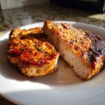 Close-up of two thick, juicy air fryer pork chops seasoned with paprika and herbs on a white plate.