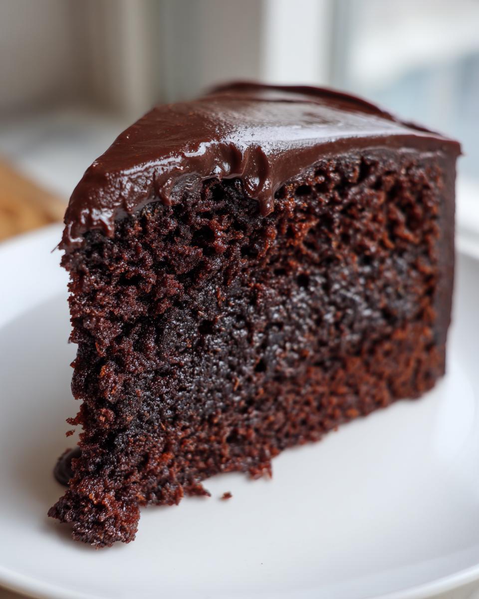 Close-up of a rich, dark slice of chocolate zucchini cake topped with glossy chocolate frosting.