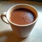 Close-up of a white mug filled with rich, frothy crockpot hot chocolate.