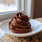 A beautiful swirl of rich, dark chocolate buttercream frosting piped onto a small white plate.
