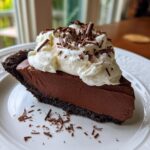 A decadent slice of french silk pie featuring a dark chocolate crust, rich filling, and topped with whipped cream and chocolate shavings.