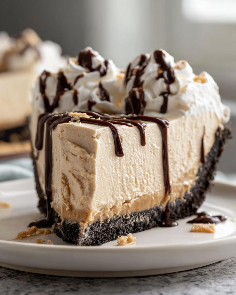 A decadent slice of no-bake peanut butter pie with a dark crust, topped with whipped cream and chocolate syrup.
