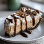 A decadent slice of peanut butter pie with a thick peanut butter filling, whipped cream, and chocolate syrup drizzle.