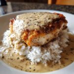 A golden-brown piece of smothered chicken and rice topped with creamy herb gravy.