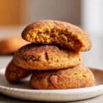 A stack of three soft, orange-hued pumpkin snickerdoodles coated in cinnamon sugar, with the top one bitten into.