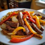 Close-up of perfectly cooked steak fajitas featuring seasoned steak strips mixed with vibrant red and yellow bell peppers and onions.