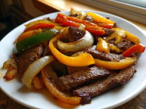 Close-up of sizzling steak fajitas featuring sliced steak, yellow, red, and green bell peppers, and caramelized onions on a white plate.