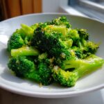 Bright green steamed broccoli florets seasoned with lemon zest and coarse salt in a white bowl.