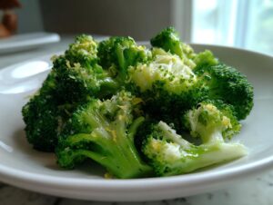 Close-up of bright green steamed broccoli florets topped with lemon zest on a white plate.