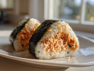 Close-up of two triangular tuna rice balls (onigiri) filled with orange tuna mixture and wrapped in dark nori seaweed.