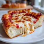 Close-up of a thick slice of cheese pizza showing a dramatic, gooey cheese pull over a white plate.