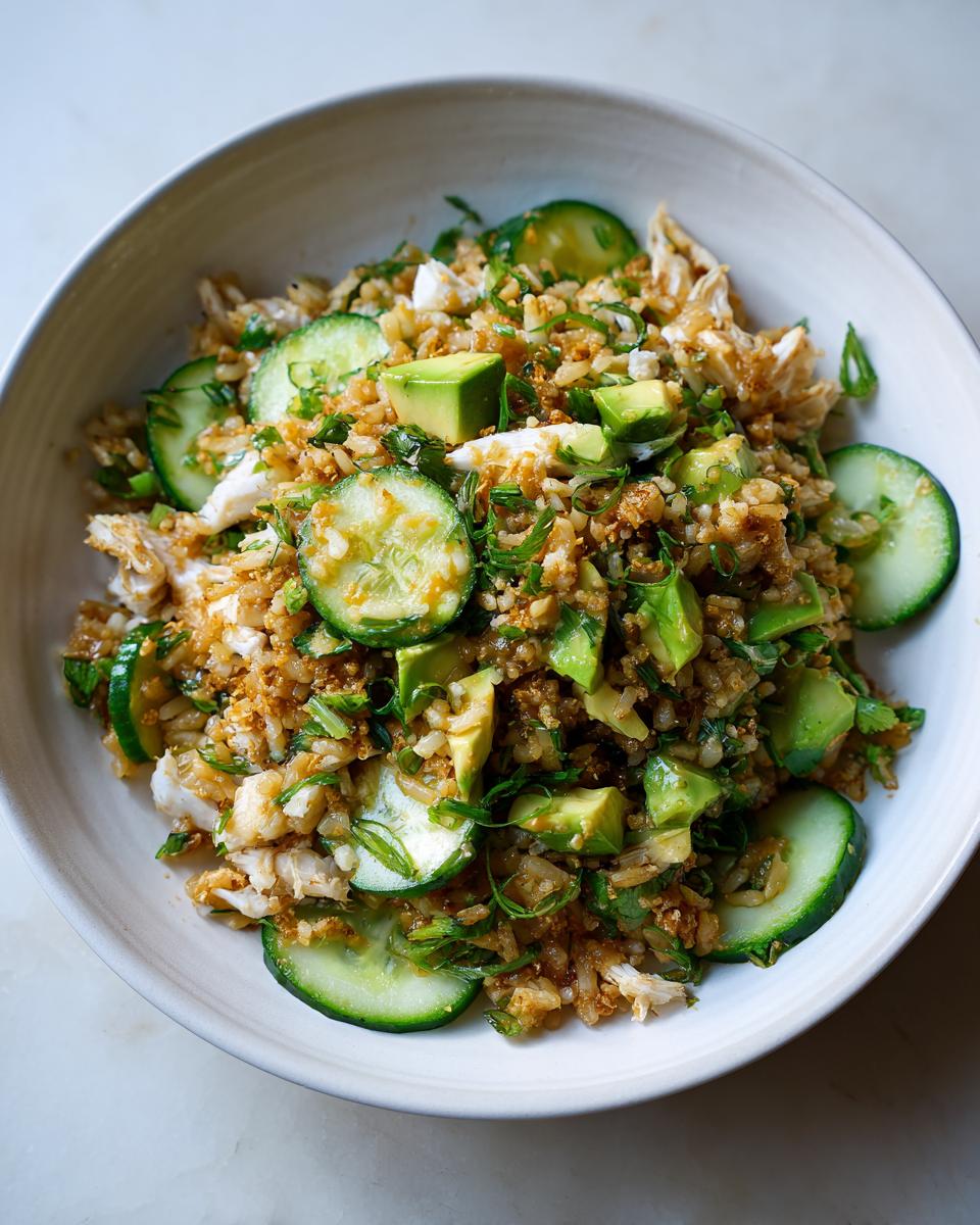 A bowl filled with flavorful crispy rice salad, mixed with chunks of avocado, sliced cucumber, and green onions.