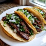Three delicious steak tacos filled with grilled, sliced steak, topped generously with chopped white onion and fresh cilantro.