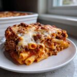 A generous slice of cheesy baked ziti covered in melted mozzarella and rich meat sauce, served on a white plate.