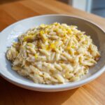 A close-up of creamy orzo pasta topped generously with bright yellow lemon zest and black pepper.