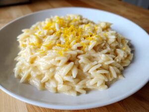 Close-up of creamy, lemon-infused orzo pasta topped with bright yellow zest in a white bowl.