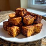 A stack of golden brown, crispy air fryer tofu cubes piled high on a white plate, ready to eat.
