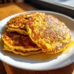 A stack of three golden brown, fluffy oatmeal pancakes topped with melting butter and drizzled with syrup.