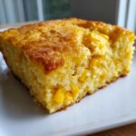 Close-up of a moist, golden slice of jiffy corn casserole studded with bright yellow corn kernels.