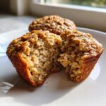 Close-up of a banana oatmeal muffin broken in half showing its moist, textured interior and oat topping.