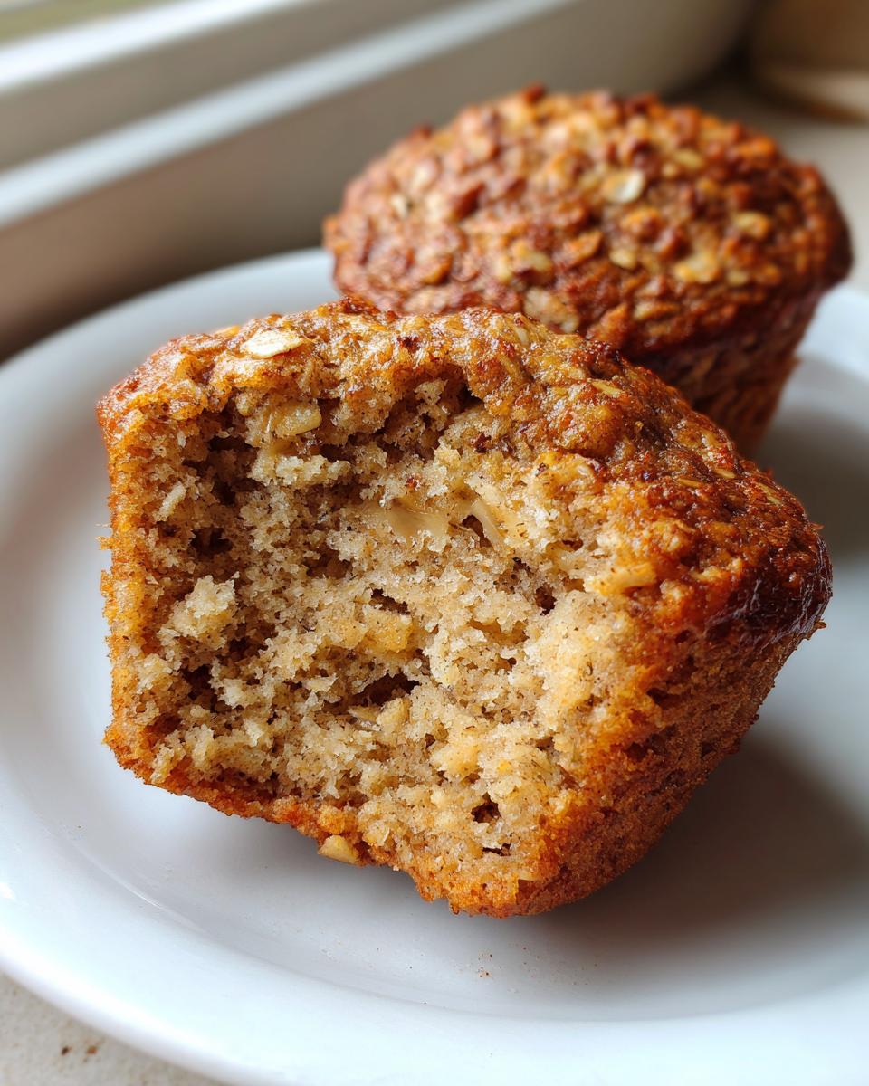 Close-up of a banana oatmeal muffin cut in half showing the moist, textured interior and oat topping.