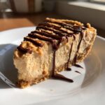 A decadent slice of no bake peanut butter pie with a thick, creamy filling and chocolate syrup drizzled over the top.