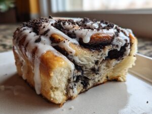 A close-up view of a single, soft Oreo cinnamon roll topped with white icing and crushed cookie pieces.