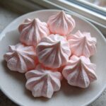 A small pile of delicate, pale pink, star-shaped meringue kisses dusted with edible glitter.