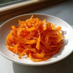 Close-up of a bright orange raw carrot salad, featuring shaved ribbons tossed with sesame seeds.